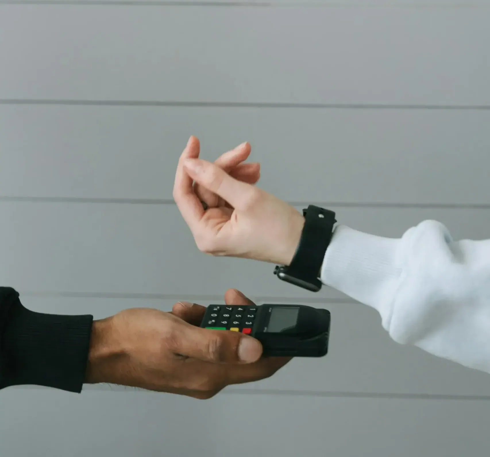 Kaviapps-woocommerce-bug-fixes-banner-image A person wearing a white sweatshirt prepares to make a payment using a smartwatch. They hold their wrist near a card reader, which is held by another person. The background consists of simple horizontal lines.